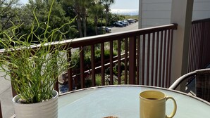 Un balcón con una mesa de vidrio, una planta en maceta, una taza y un plato con galletas.