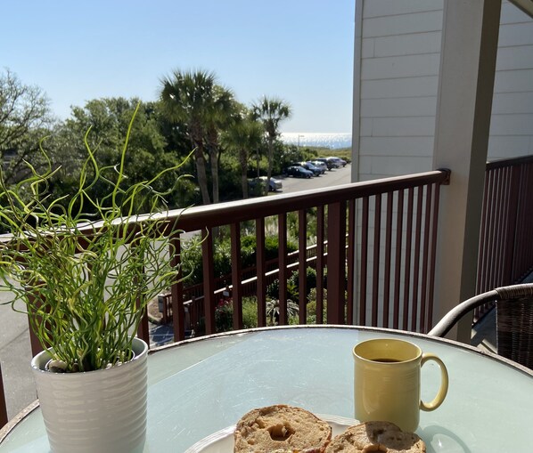 A balcony with a glass table, a potted plant, a mug, and a plate with cookies.