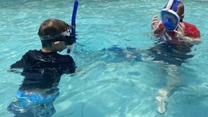 Una piscina con dos niños en el agua, uno con máscara y tubo de snorkel y el otro con un flotador.