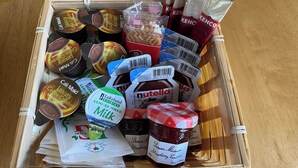 Verschiedene Lebensmittel wie Kaffeesahne, Nutella, Milch und Erdbeermarmelade in einer Holzkiste.