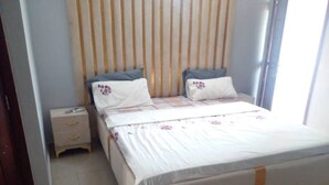 A bedroom with a bed, two pillows, a nightstand, and a window with blinds. - Lovely 1-Bed duplex house (BINGERVILLE)