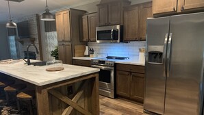 A modern kitchen with wooden cabinets, stainless steel appliances, and a marble island. - Robin’s Nest Cabin- quiet cove on Lake Hamilton (Hot Springs National Park)