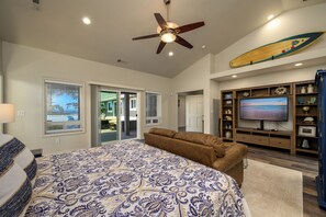 A bedroom with a large bed, a ceiling fan, a TV, and a surfboard on the wall.