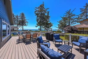 A wooden deck with outdoor furniture, a grill, and a view of the ocean.