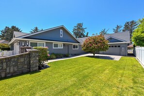 A residential house with a stone wall, a well-maintained lawn, and a tree with pink flowers.