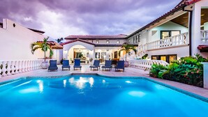 Une piscine avec des chaises longues, un patio couvert et un bâtiment doté d’un toit en tuiles.