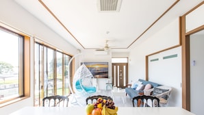 A spacious room with a dining table set with fruit, a hanging chair, and a sofa with cushions. - West coast villa Shirahama (Shirahama)