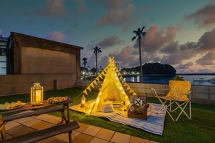 A picnic setup with a tent, table, and chairs on a terrace overlooking a body of water.