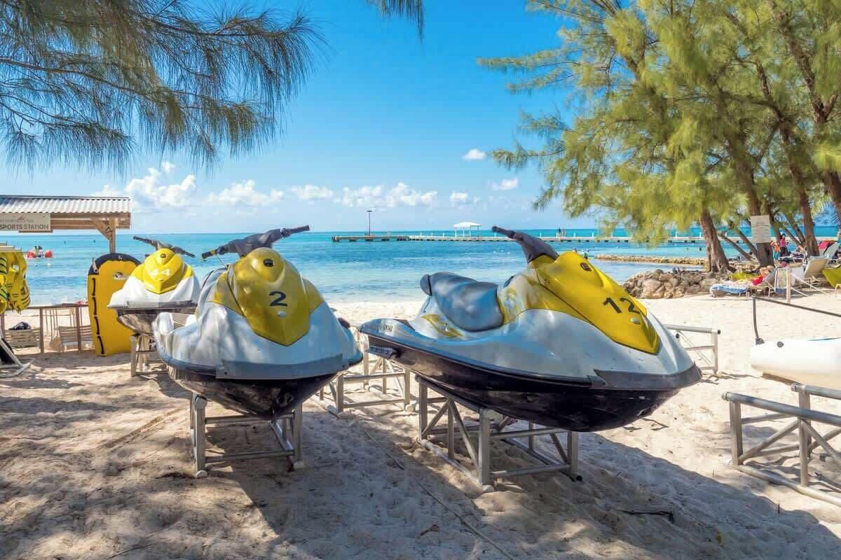 Jet skis on a sandy beach with a clear view of the ocean and a pier in the background.