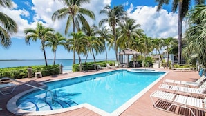 A swimming pool with lounge chairs, palm trees, and a view of the ocean. - Kaibo Kai Hacienda B-5 2BR/2BA at Scenic Kaibo Kai -- Beach & Pool (Cayman Kai)