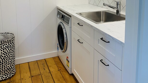 A laundry room with a washing machine, a sink, and cabinets. - Meryta House (Norfolk Island)