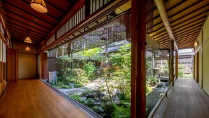 A traditional Japanese-style corridor with wooden flooring and a view of a garden through a glass partition. - RESI STAY Shinshinen (Kyoto)