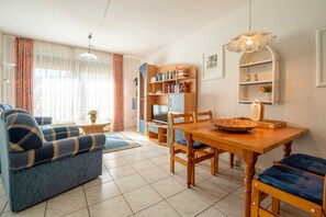 Een woonkamer met een bank, een eettafel, een televisie, een boekenkast en een hanglamp.