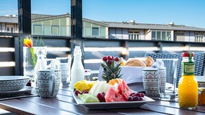 A breakfast table with a variety of fruits, a bottle of orange juice, and a croissant on a balcony overlooking a building. - Hotel am Stadtpark (Hilden)