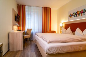 A hotel room with a bed, desk, chair, and a painting of birds on the wall. - Hotel am Stadtpark (Hilden)