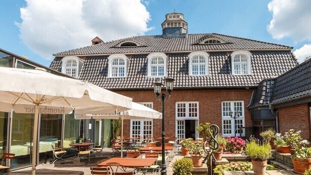 A traditional brick building with a tiled roof, outdoor seating area with tables and chairs, and potted plants. - Hotel am Stadtpark (Hilden)