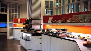 A modern kitchen with white cabinets, a curved countertop, and a variety of food items and kitchenware. - Hotel am Stadtpark (Hilden)