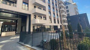 Un edificio de varios pisos con un diseño arquitectónico moderno, con balcones, ventanas amplias y una entrada protegida por un portón.