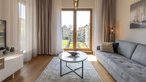 Una sala moderna con un sofá, una mesa de centro de vidrio y vistas de un paisaje urbano a través de amplios ventanales.