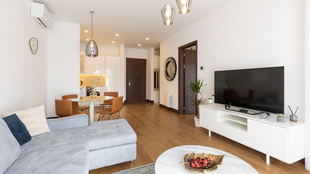 Una sala de estar moderna con un sofá, una zona de comedor y un televisor sobre un mueble blanco.