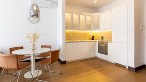 Una cocina moderna con armarios blancos, una mesa redonda de vidrio y sillas anaranjadas.