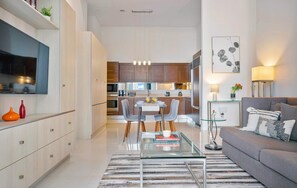 A modern living room with a glass coffee table, grey sofa, and a dining area with chairs and a table.