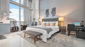 A modern hotel room with a large bed, a desk, and a view of the city.