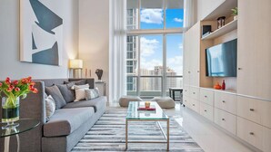 A modern living room with a grey sofa, a glass coffee table, and a large TV on a wooden cabinet.