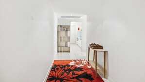 A narrow hallway with a red and black patterned rug, a wooden console table, and a white shelving unit against the wall.