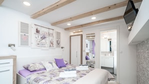 A bedroom with a bed, a dresser, a mirror, and a TV mounted on the wall. - Lavender Room (Dubrovnik)