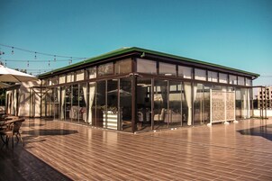 A covered outdoor seating area with a wooden deck, glass walls, and a green roof.