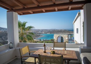 A wooden table with chairs on a balcony overlooking a coastal view with buildings and a clear sky.
