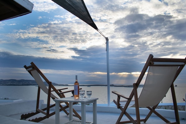 A terrace with two wooden chairs and a table, a bottle, and two glasses on the table.