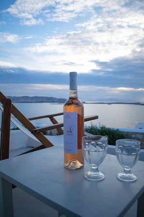 A bottle of wine and two glasses on a table with a scenic view of a body of water and mountains in the background.
