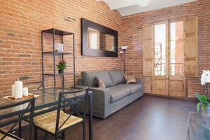 A living room with a brick wall, a grey sofa, a glass coffee table, and a wooden door. - 2-bedroom Apartment for Families (Barcelona)