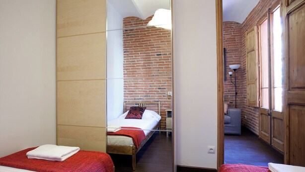 Una habitación con dos camas, una pared de ladrillo y un espejo que refleja el interior.