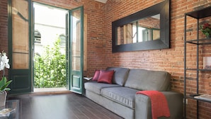A living room with a grey sofa, red cushions, a red throw blanket, a black-framed mirror, and a potted plant. - Family Apartment Near Sagrada Familia (Barcelona)
