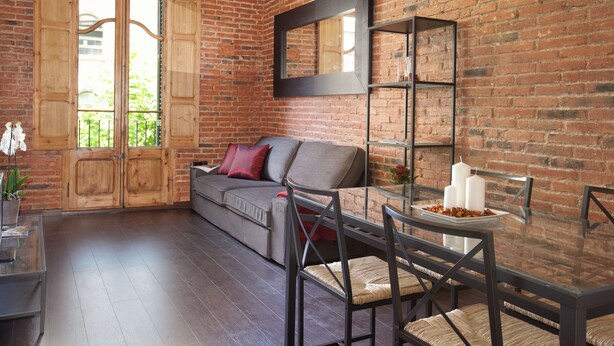 Ein Zimmer mit Backsteinwand, einer Couch, einem Glastisch mit Kerzen und einem Spiegel.
