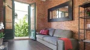 Ein Wohnzimmer mit grauem Sofa, roten Kissen, einer roten Decke, einem spiegeln Spiegel mit schwarzem Rahmen und einer Topfpflanze.