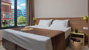 Ein Hotelzimmer mit einem großen Bett, zwei Nachttischen, einem Fenster mit Blick auf Gebäude und einer kleinen Pflanze auf einem Tisch.