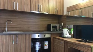 Eine moderne Küche mit Holzausstattung, einer Edelstahl-Spüle, einer Mikrowelle, einem Wasserkocher und einem Backofen.