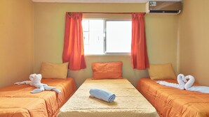 Hotelkamer met twee bedden, oranje beddengoed, een centraal bed met een opgerolde handdoek, en een raam met oranje gordijnen.