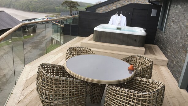 Ein Balkon mit Korbmöbeln, einer Whirlpool und Blick auf eine Straße und Bäume.