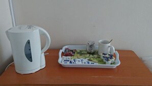 Una tetera blanca, una bandeja con comida y condimentos, y una taza sobre una mesa de madera.