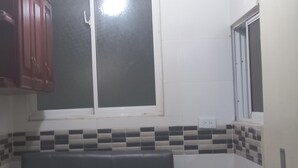 A kitchen with a window, a tiled backsplash, and a wooden cabinet. - Room-single Room With Queen Bed Near SDQ (Santo Domingo Este)