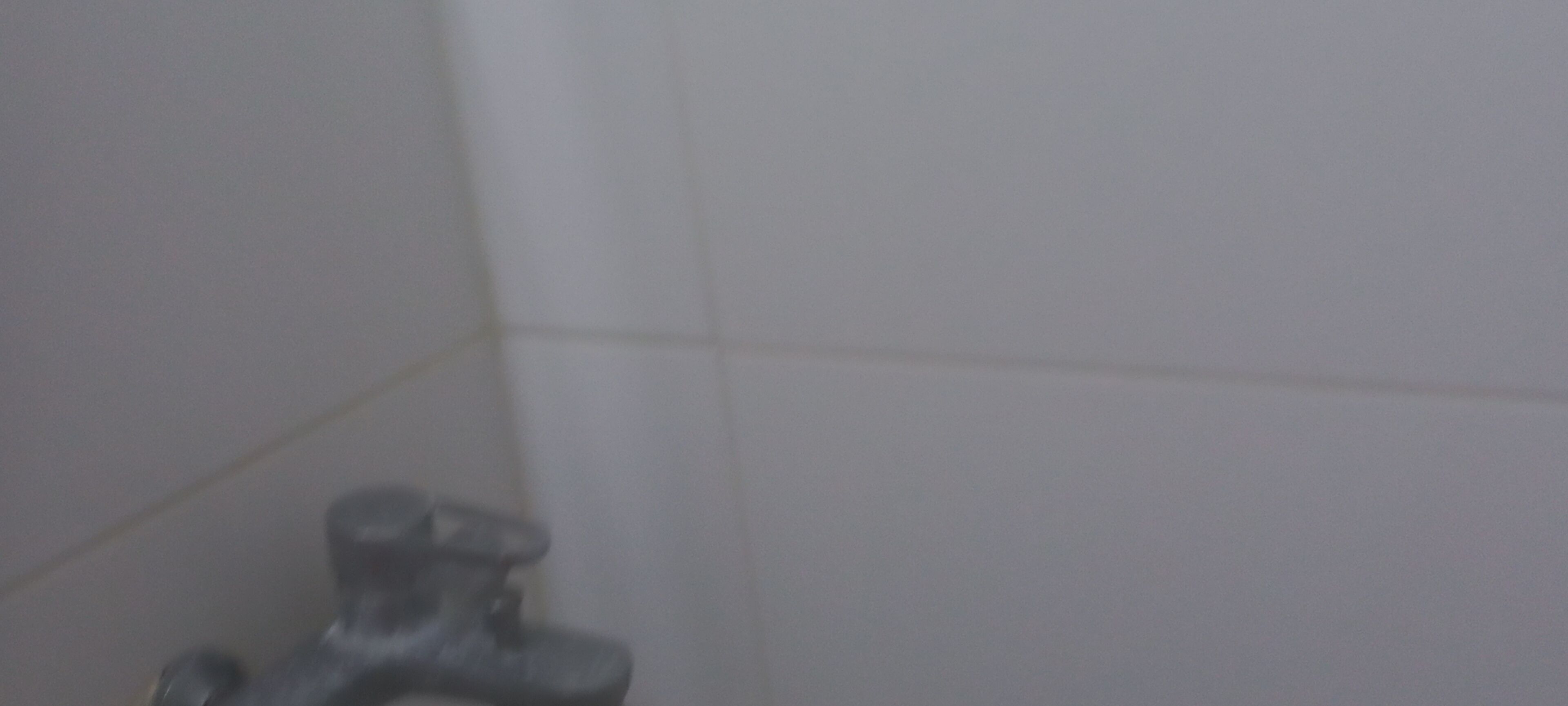 A bathroom with white tiles, a visible shower area, and a faucet.
