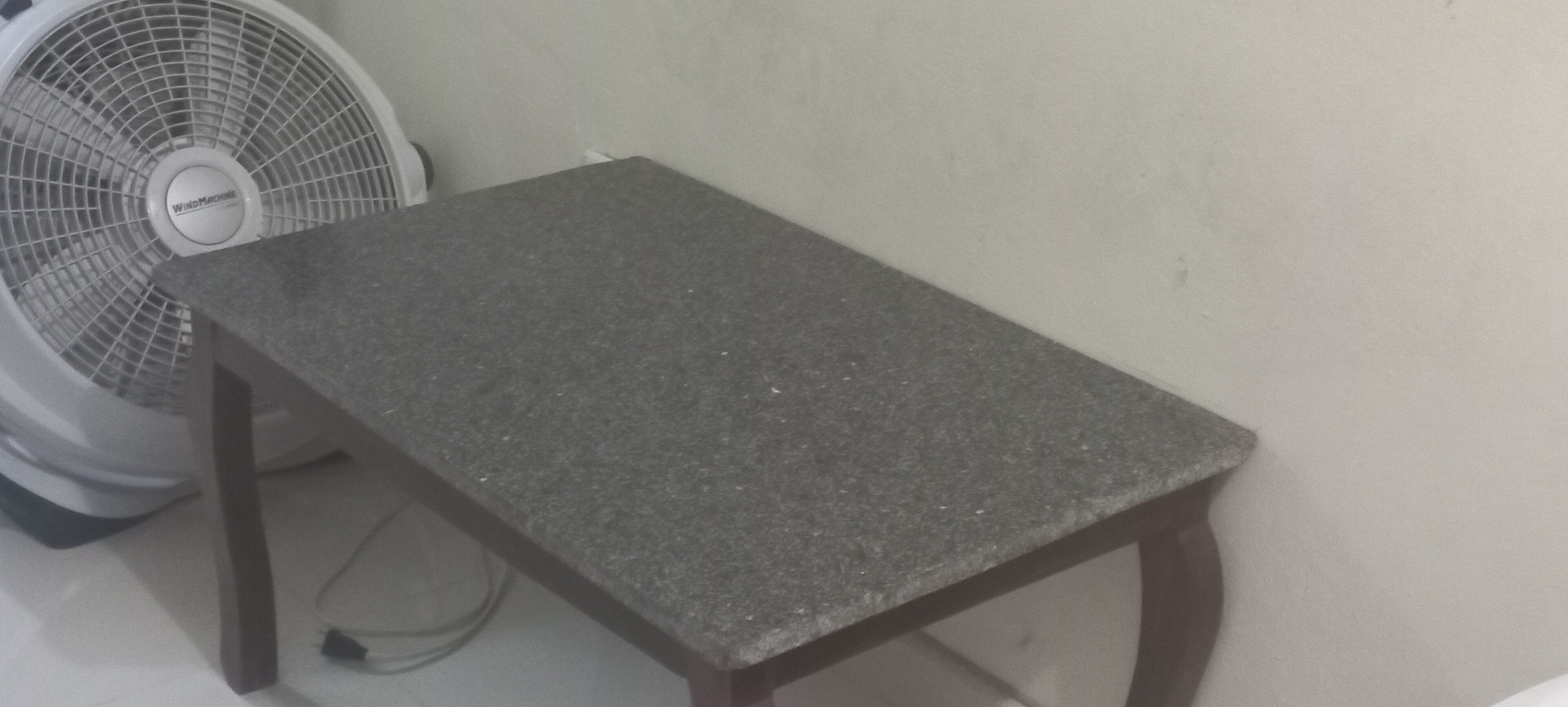 A small table with a dark surface and wooden legs, positioned next to a standing fan.