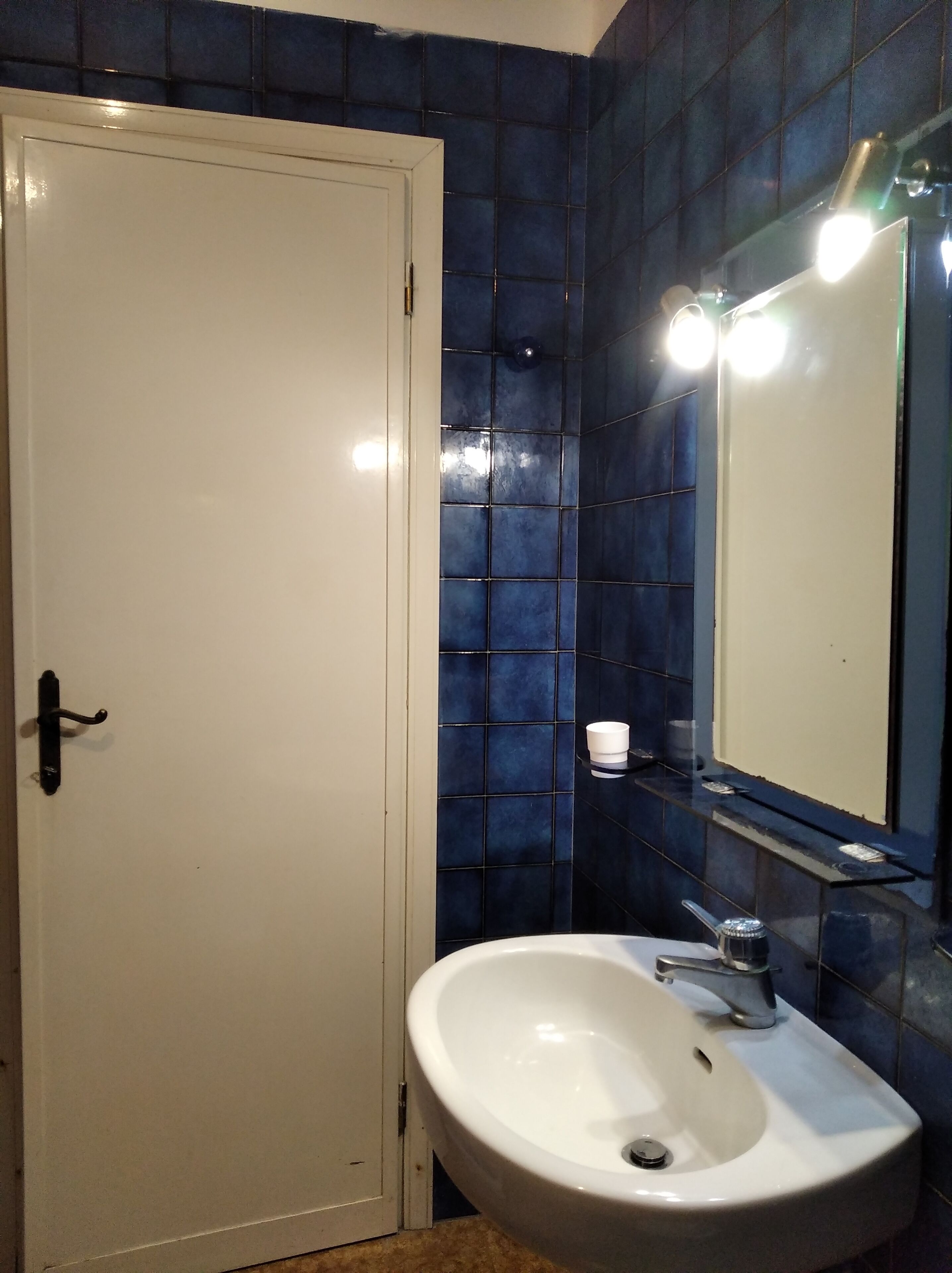 Ein Badezimmer mit einem weißen Waschbecken, einem Spiegel und blautonierten Fliesen.