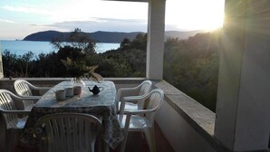 A balcony with a table and chairs overlooking a scenic view of a body of water and hills. - Villa With Garden and Terrace for 8 pax (Capoliveri)