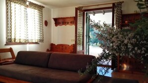 A living room with a sofa, a wooden chair, a wooden shelf with decorative items, and a potted plant. - Villa With Garden and Terrace for 8 pax (Capoliveri)